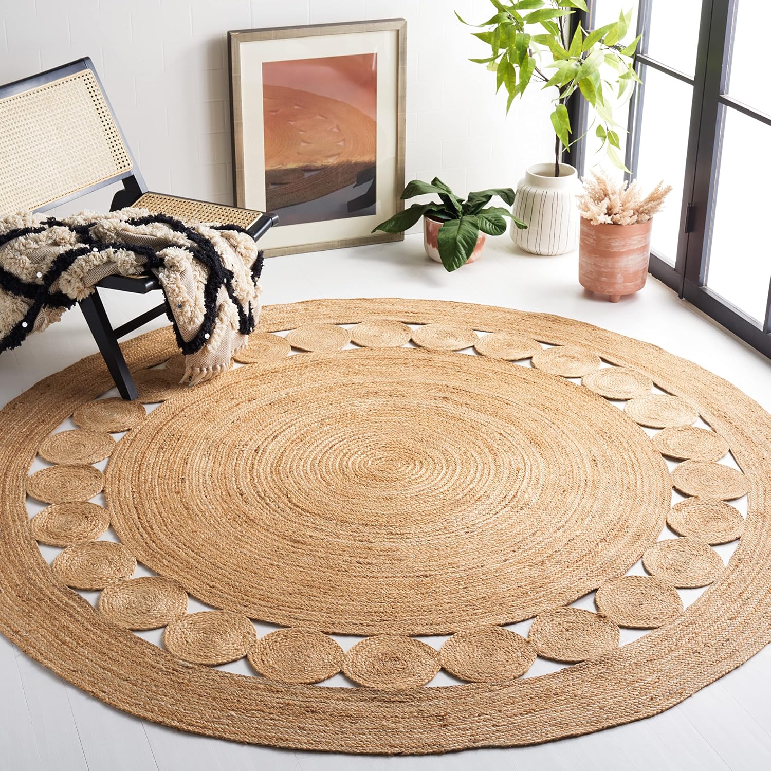 Round jute rug with a circular pattern, next to a chair, potted plants, and a framed picture